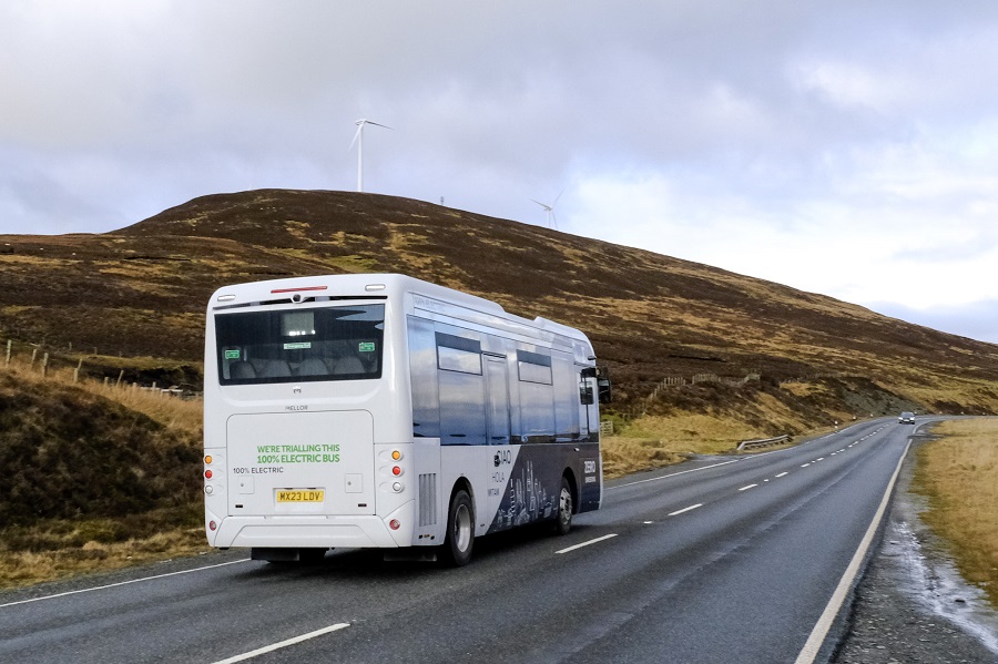 A white electric bus travels along a shetland road