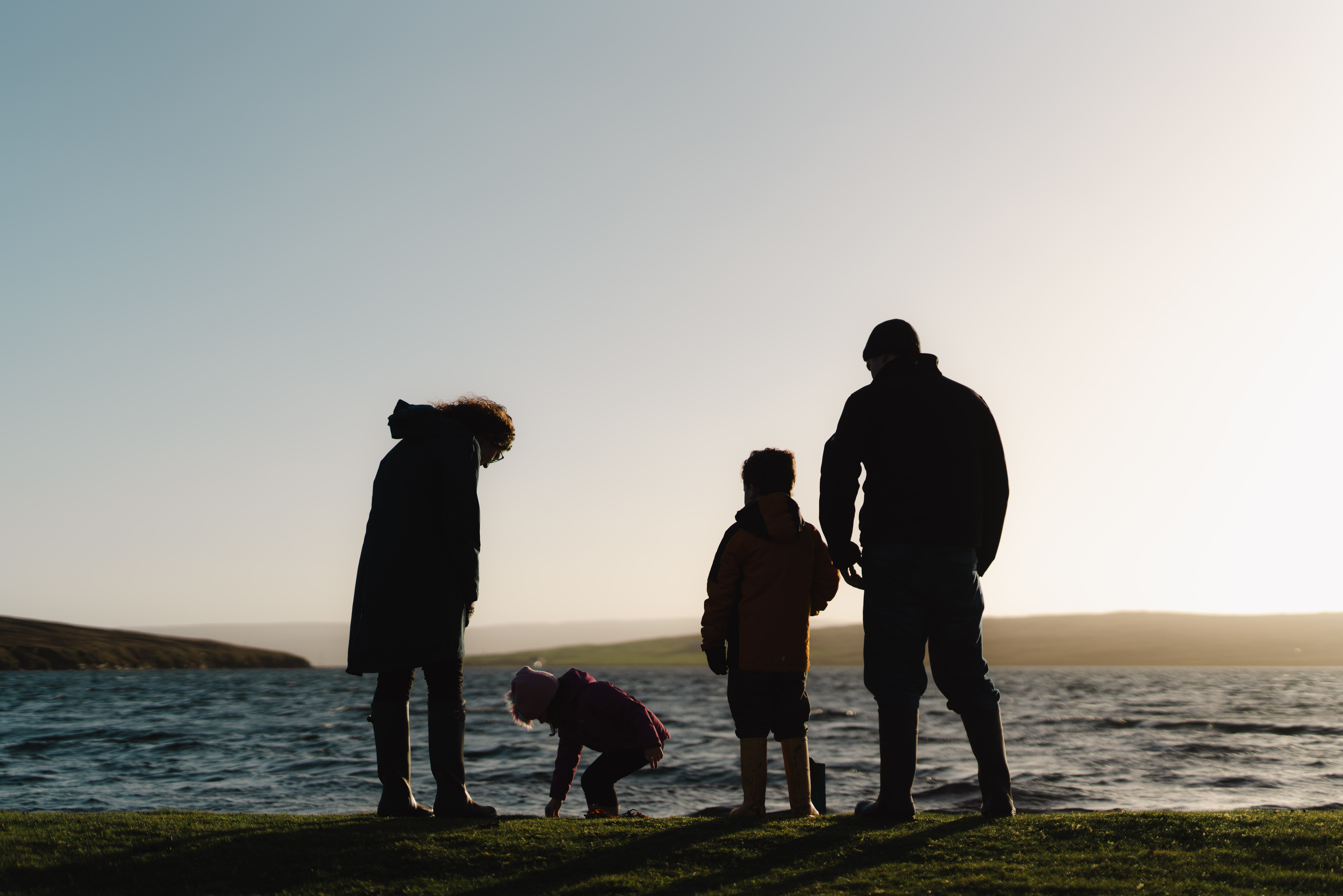 A family of four in silhoutte on a Shetland beach, the sky is moody and dramatic