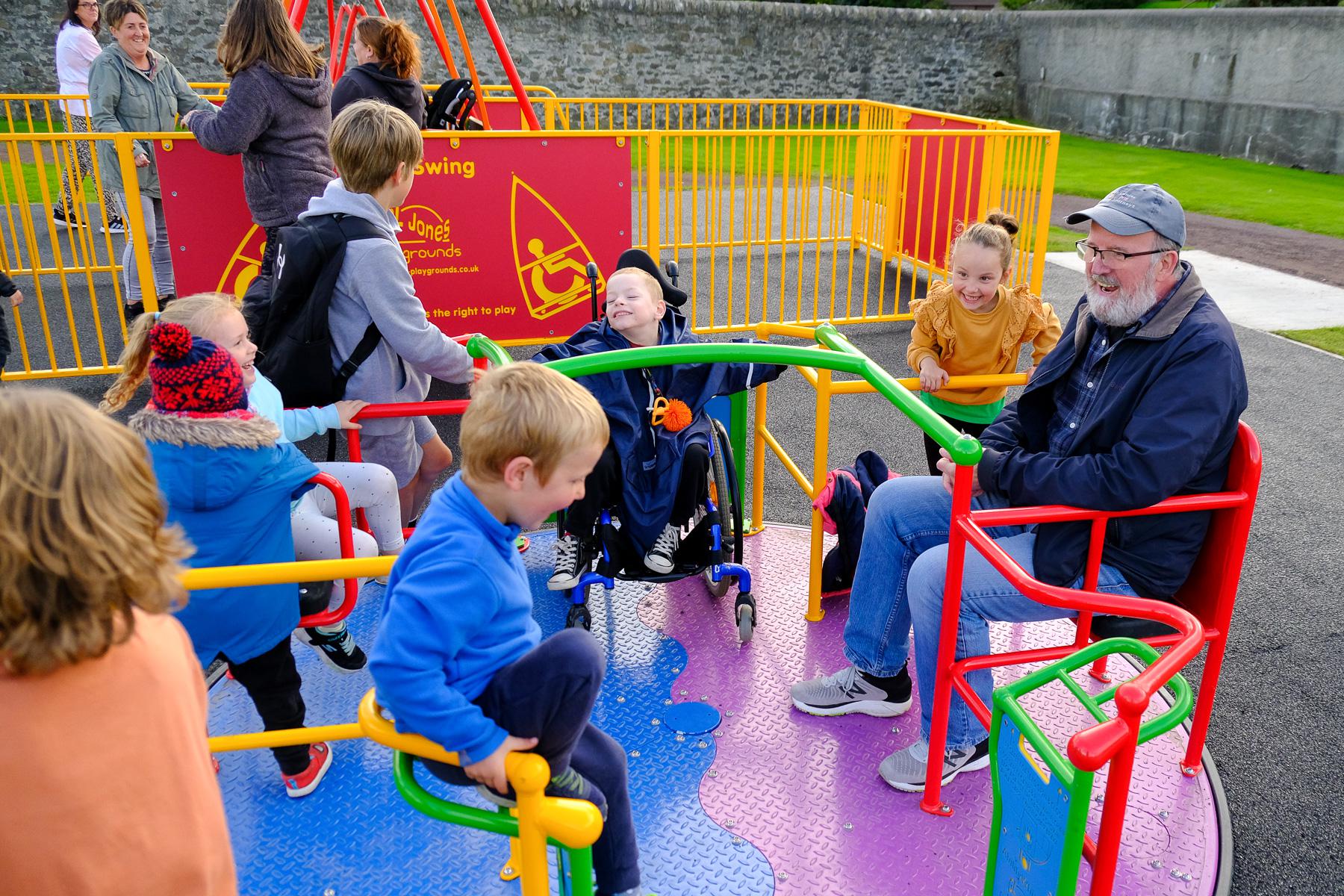 Councillor Davie Sandison (right) enjoys a birl with the bairns on the new ability roundabout at King George V play area in Lerwick.  Credit: SIC