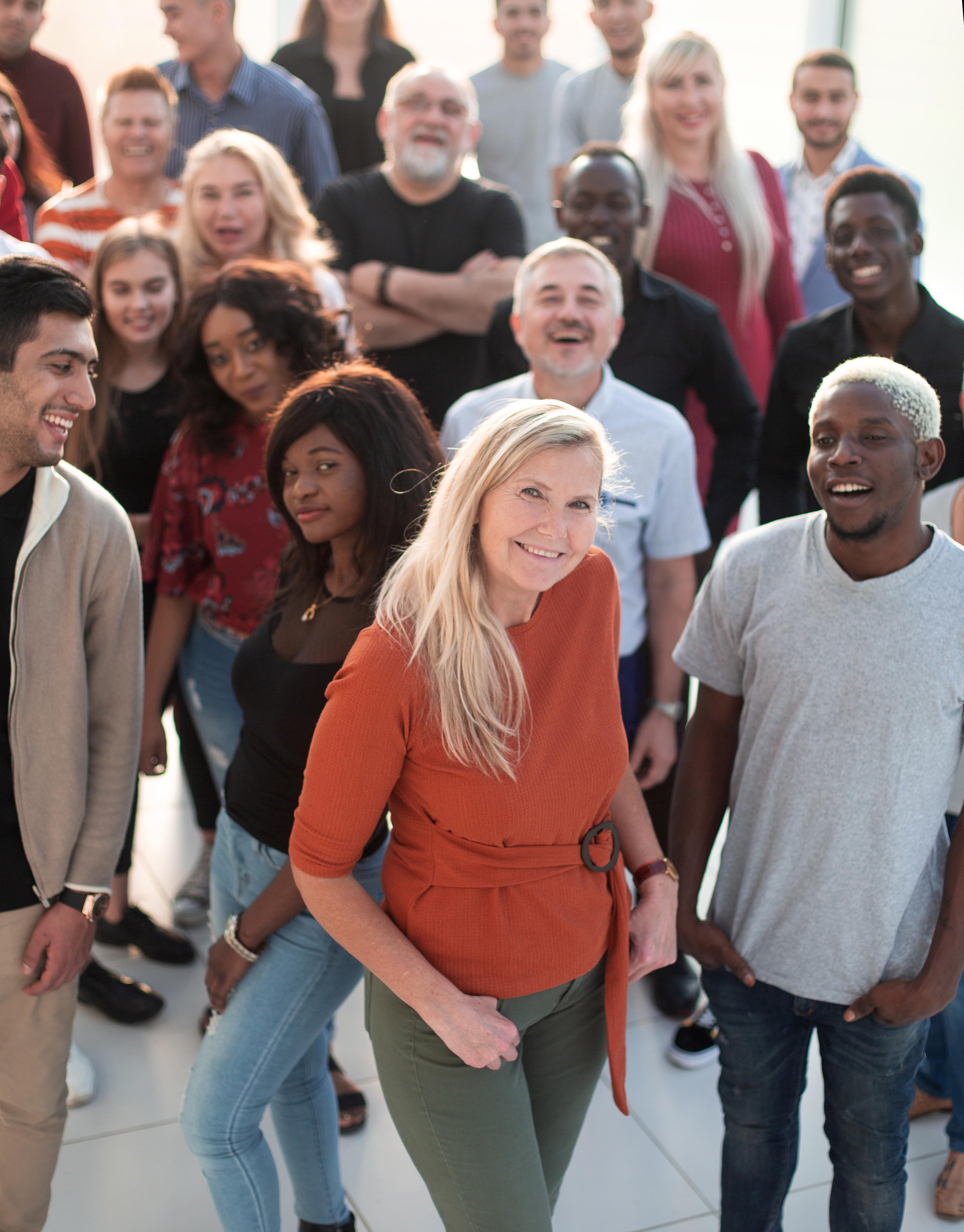 Picture shows a large diverse group of people standing together, smiling at the camera. The people are wearing a variety of different clothes.