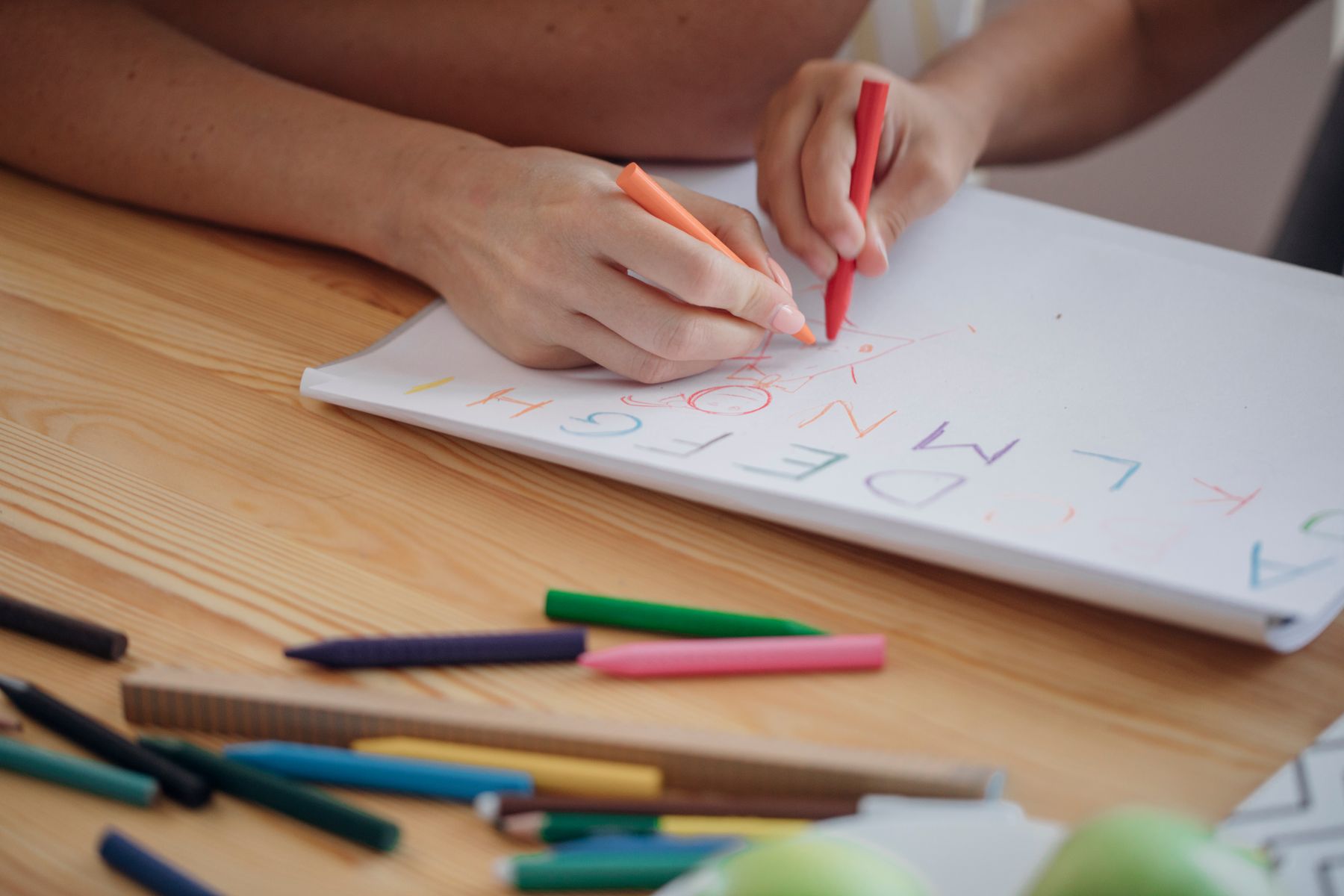 A child and adults hand working on writing with crayons