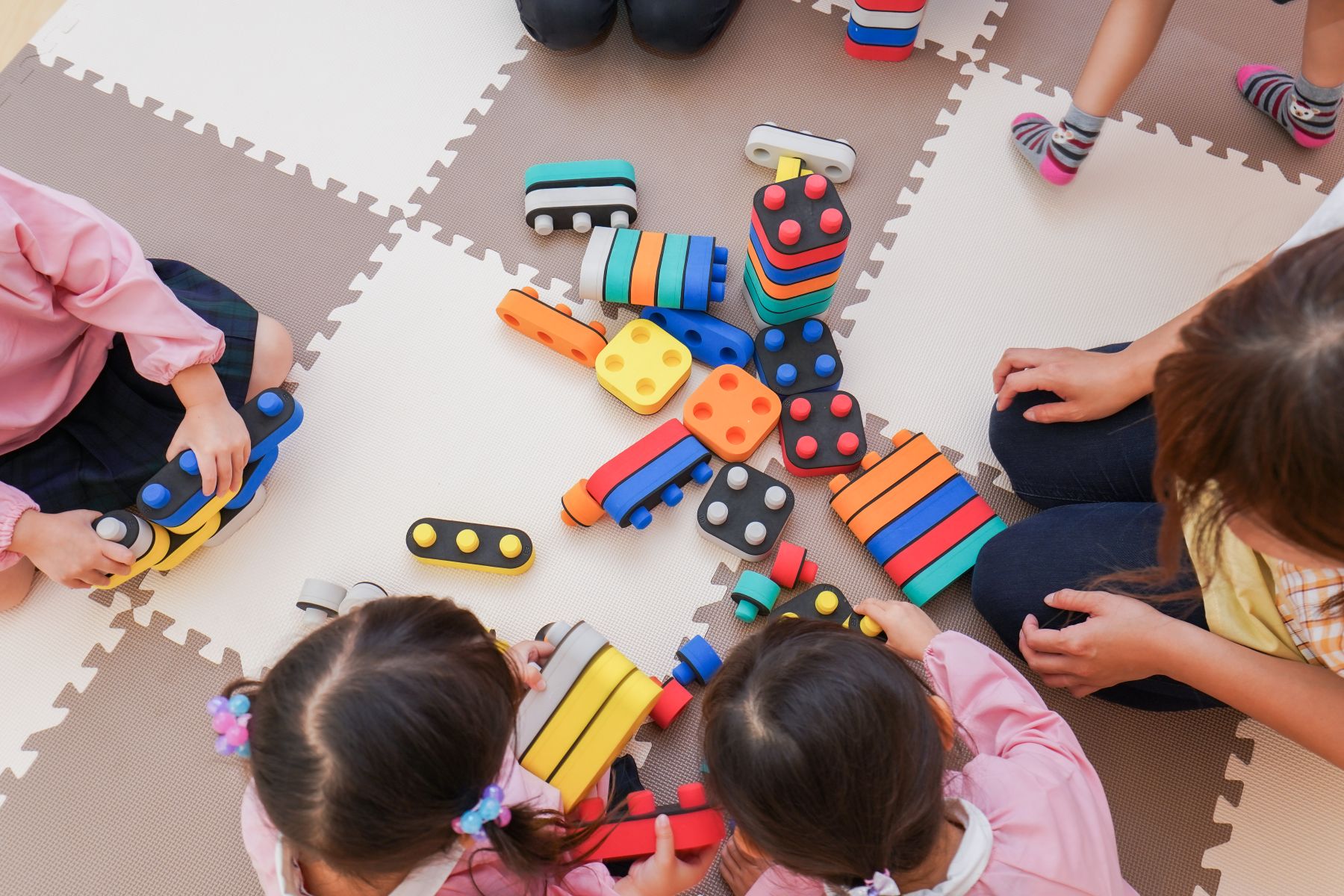 Image taken from above of four children playing with coloured bricks on a chequerboard mat