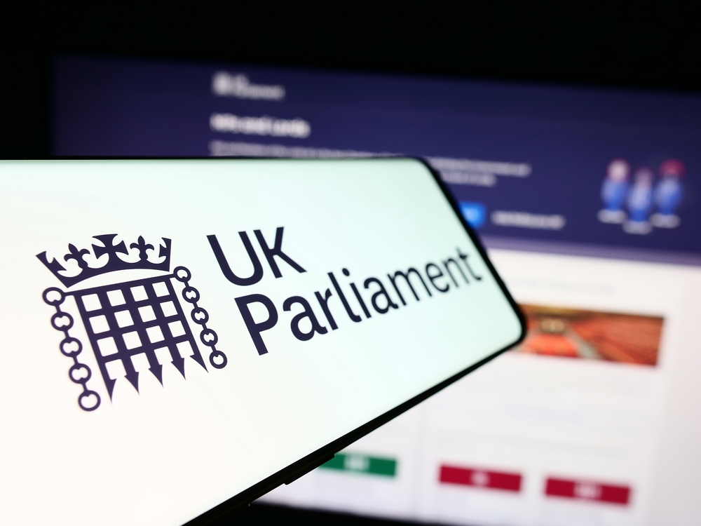 Image of a UK Parliament logo on a mobile phone in front of a computer screen