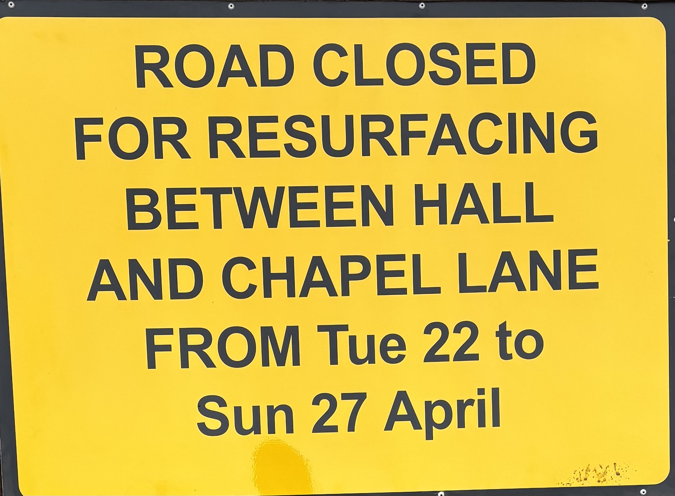 Sign reads Road closed for resurficing between hall and chapel lane from teu 22 to sun 27 april